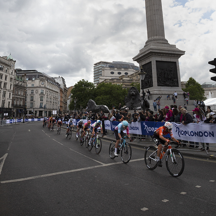 RideLondon Classique 2022 - A strung out group of riders speed through Trafalgar Square past Nelson’s Column